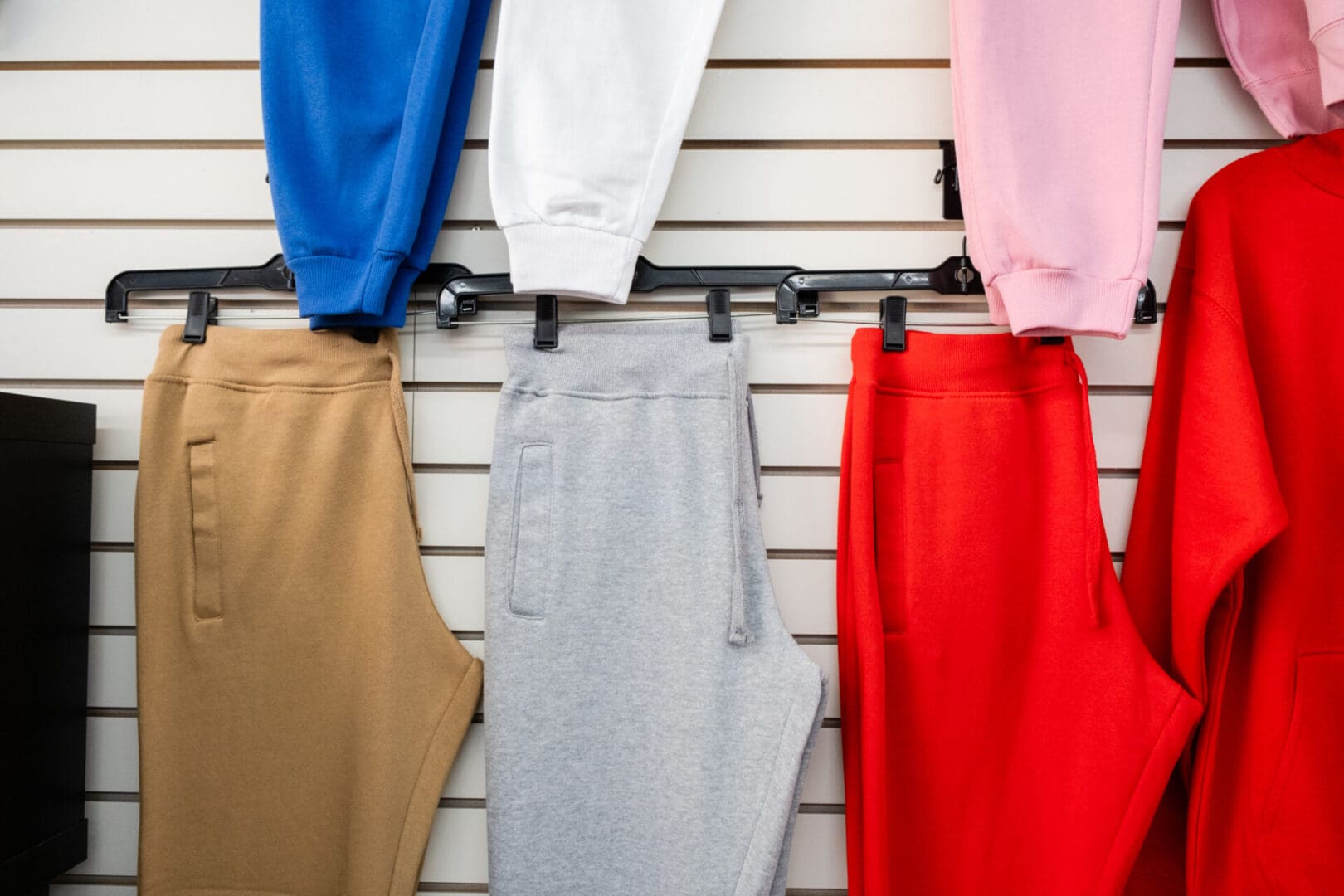 A wall with several different colored sweatpants hanging.