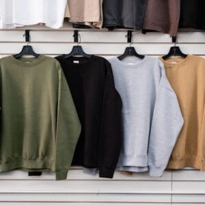 A row of different colored sweatshirts hanging on clothes racks.