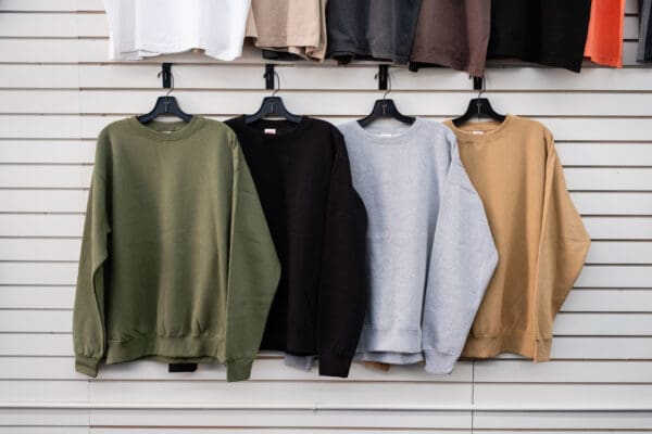 A row of different colored sweatshirts hanging on clothes racks.